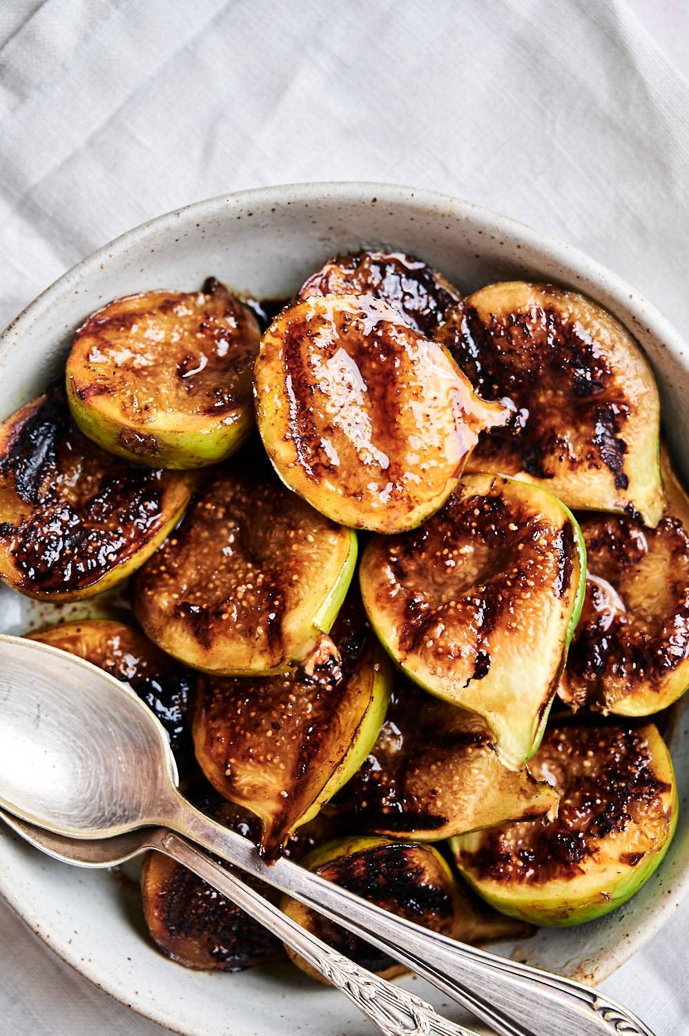 Tender grilled figs with balsamic vinegar in a bowl with two spoons.