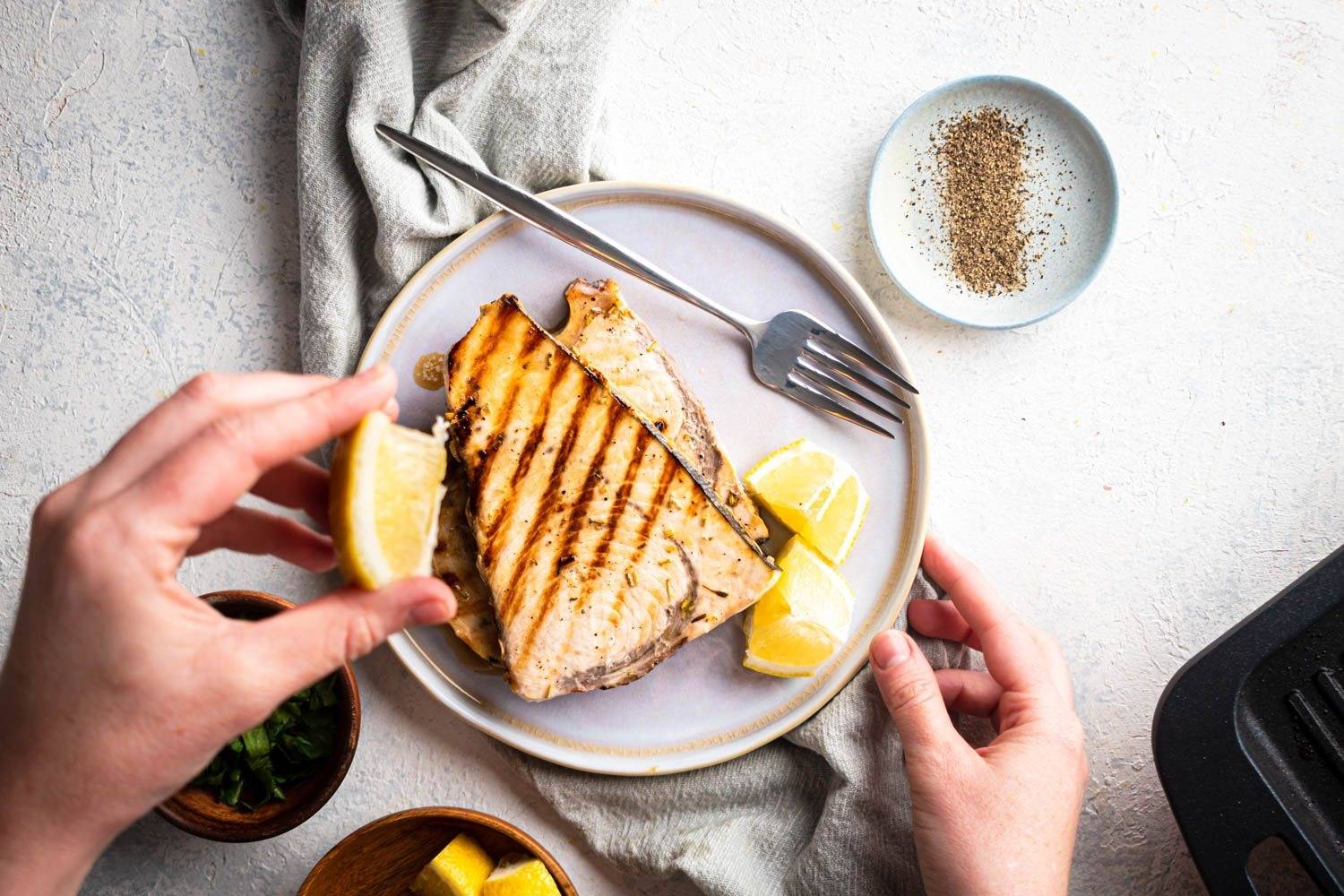 Grilled lemon swordfish steak, garlic, pepper and herbs on a plate with fresh lemon slices.