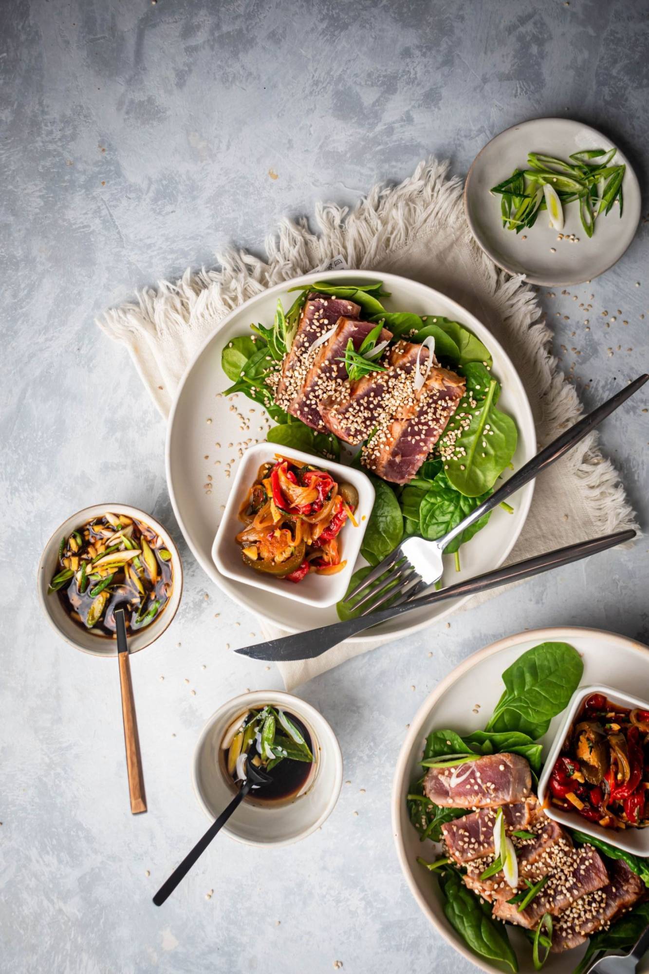 Bake slices of asi tuna, sesame, soy sauce and green onions on two plates with greens.