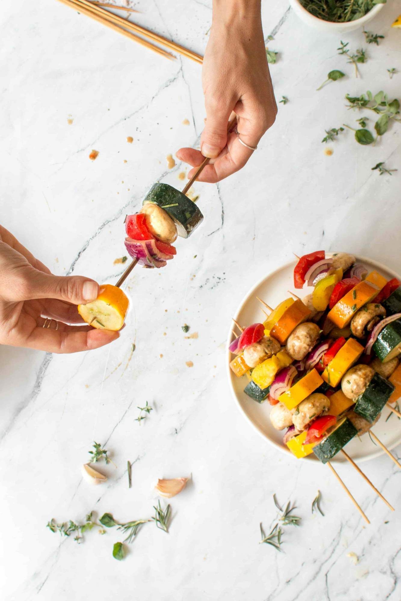 Theading vegetable skewers for the grill with mushrooms, zucchini, red onion, and bell peppers.