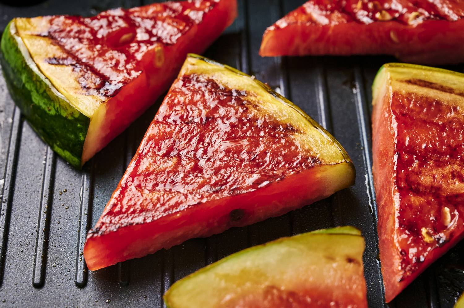 Sliced grilled watermelon with grill marks on a flat top grill.
