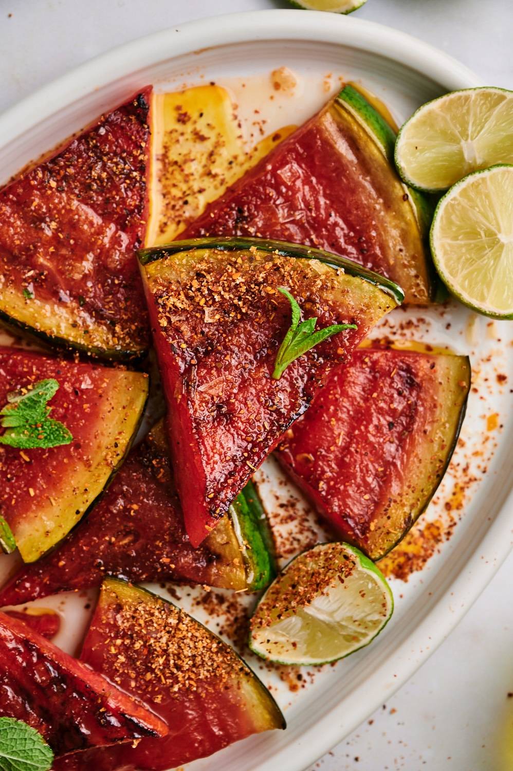Grilled watermelon slices served with chili powder, lime juice, and fresh mint on a platter.