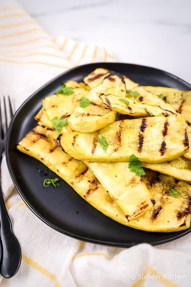 Baked yellow summer pumpkin with barbecue marks on a plate with yellow napkin.