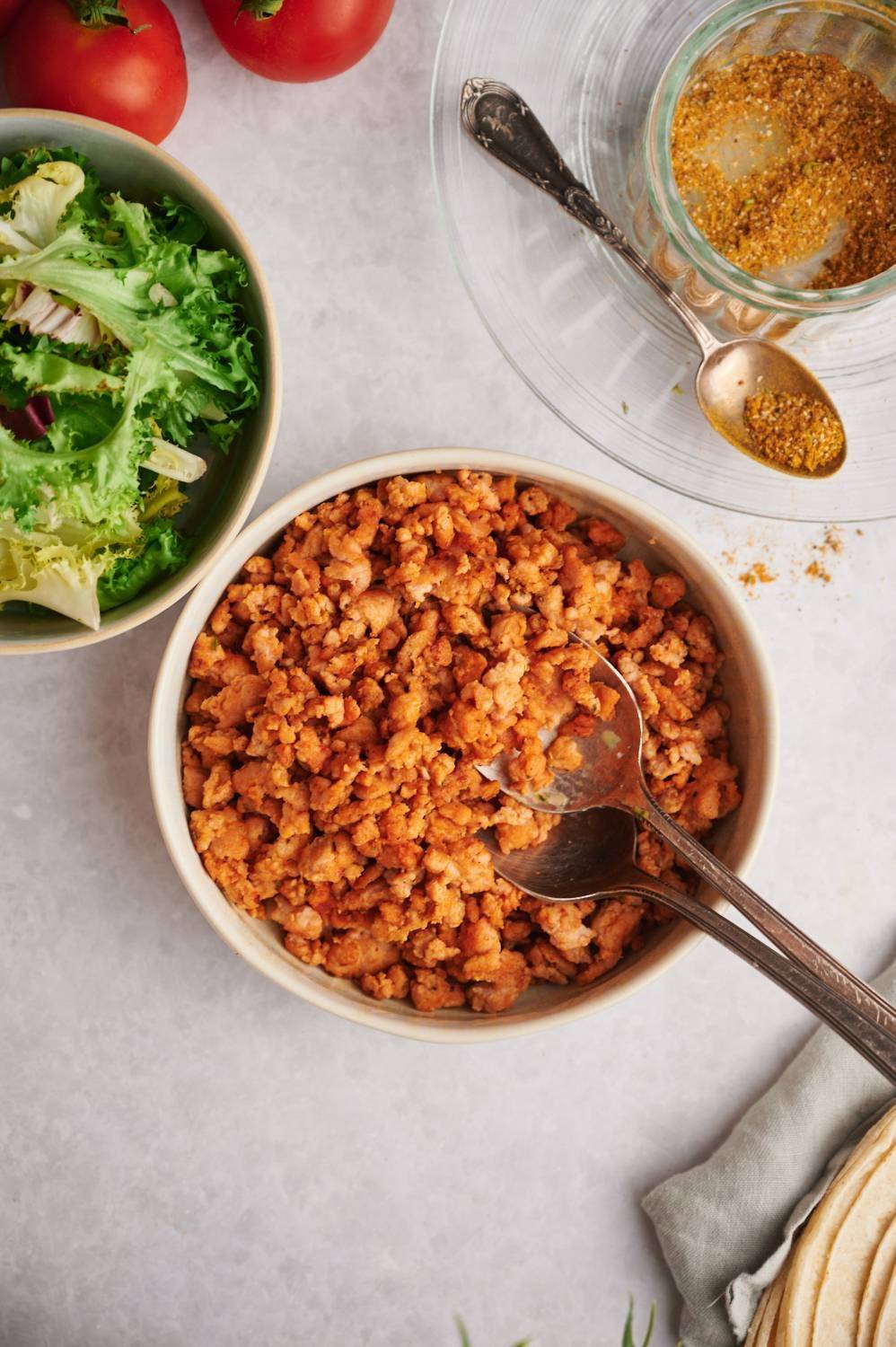 Tacos season the chicken in a bowl with homemade seasonings, lettuce and tomatoes on the sides.