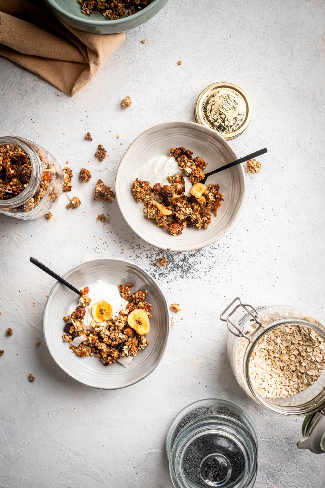 Homemade healthy granola served in two bowls with Greek yogurt, hazelnuts, and dried bananas,