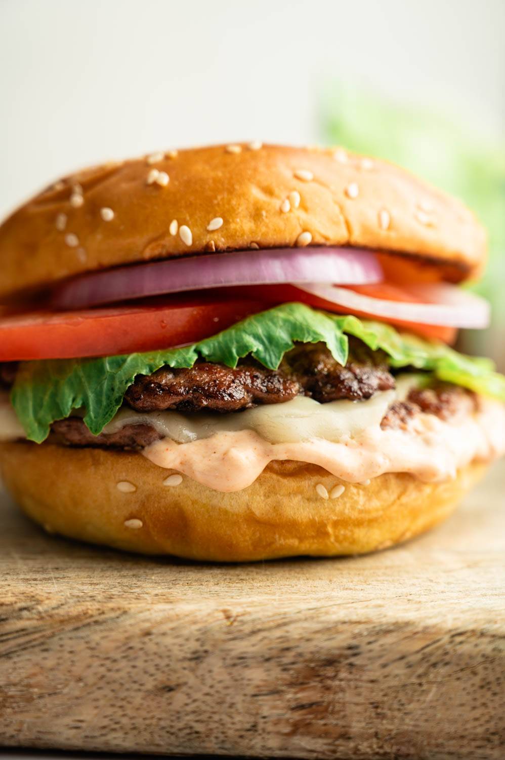 Close-up of a healthy smash burger topped with melted cheese, lettuce, tomato, red onion, and creamy special sauce on a sesame seed brioche bun.