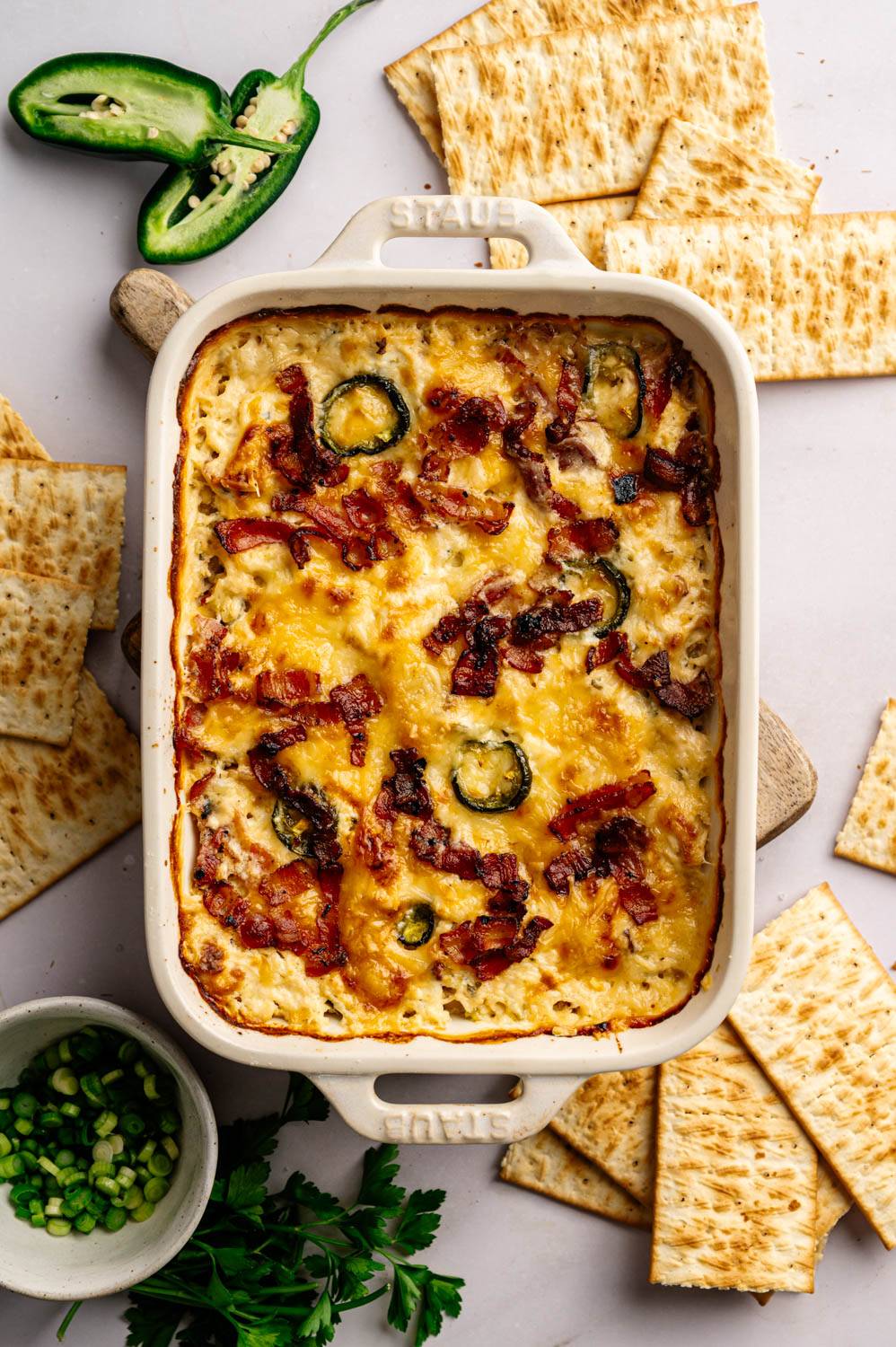 Baked casserole topped with melted cheese, bacon and jalapeño slices, surrounded by tortilla chips. Place a small bowl of chopped scallions and parsley on the side.