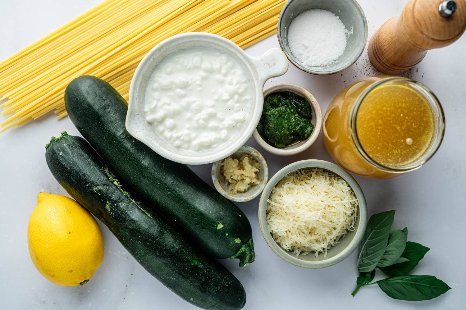 Overhead shot of finished zucchini pasta in a stainless steel pan, garnished with grated Parmesan, chopped parsley, and cracked black pepper, with linguine and zucchini half moons coated in a creamy sauce.