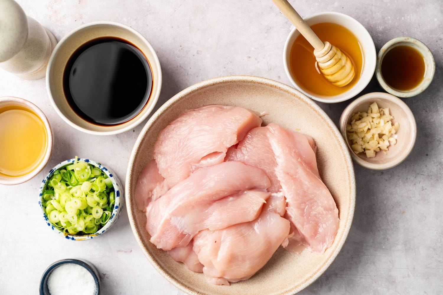 Place raw chicken breast slices in a bowl, surrounding with chopped garlic, scallions, soy sauce, vinegar, honey and spices, and place on a light surface.