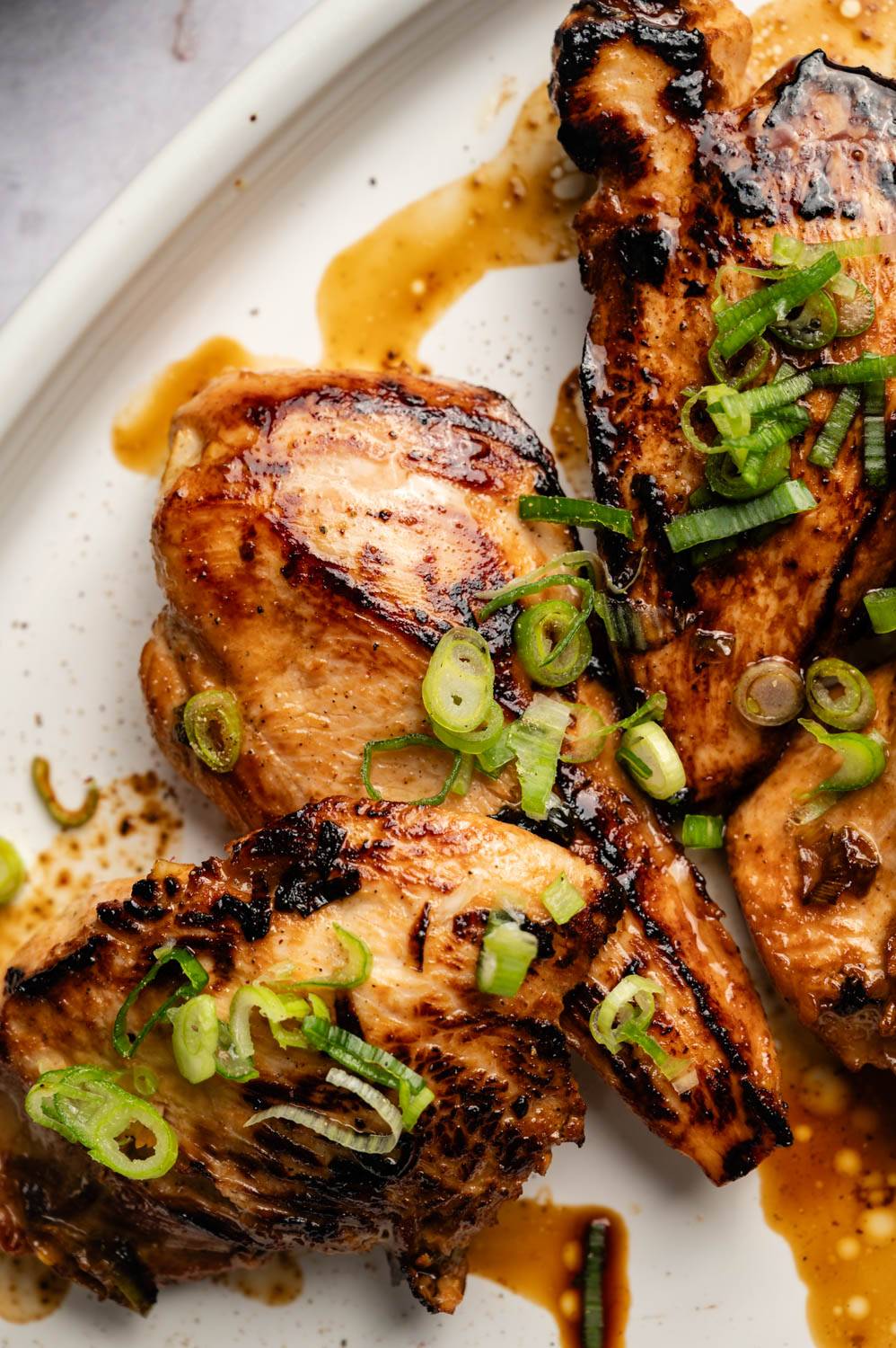 Grilled chicken wings, served with sliced ​​green onions, served on a white plate, drizzled with sauce, fragrant.