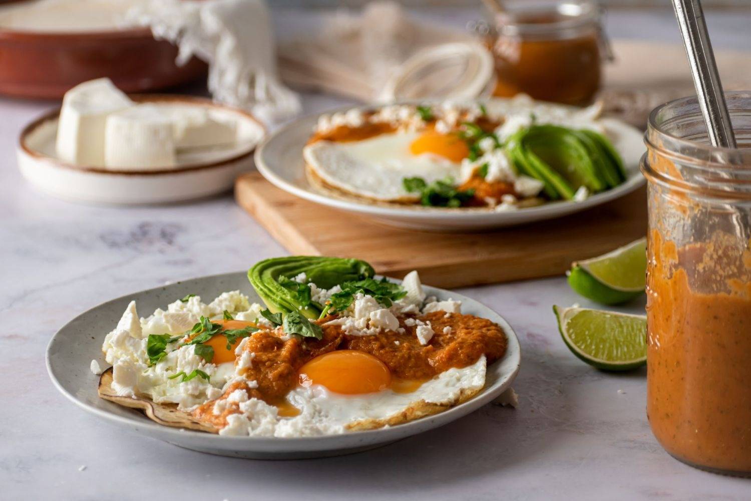 Homemade Huevos Rancheros are served on two plates with avocado, Ranchero sauce, Queso Fresco and cilantro.