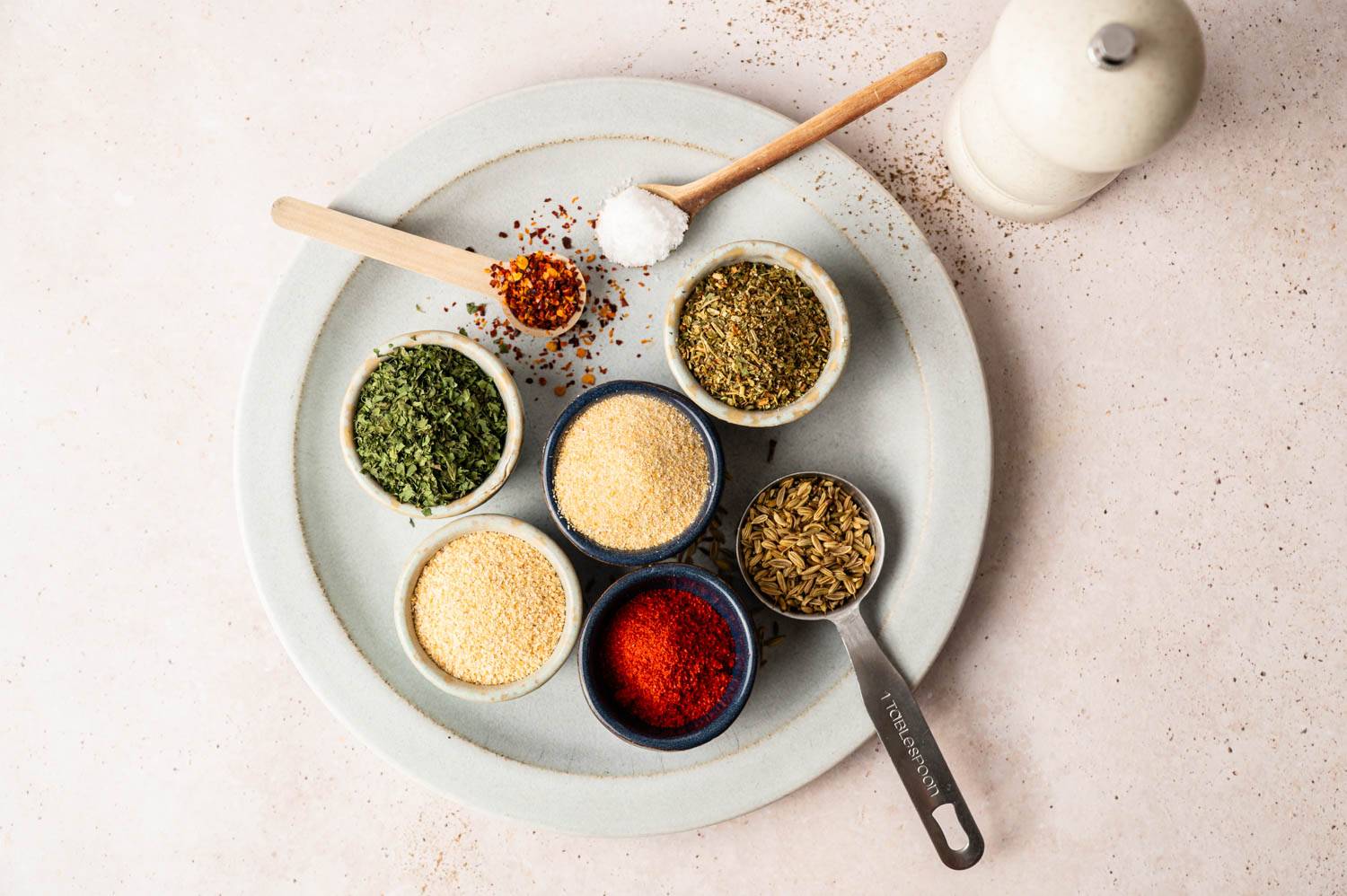 A disc holds a bowl of various spices, including dried herbs, garlic powder, paprika and fennel, along with small wooden spoons and a salt shaker.