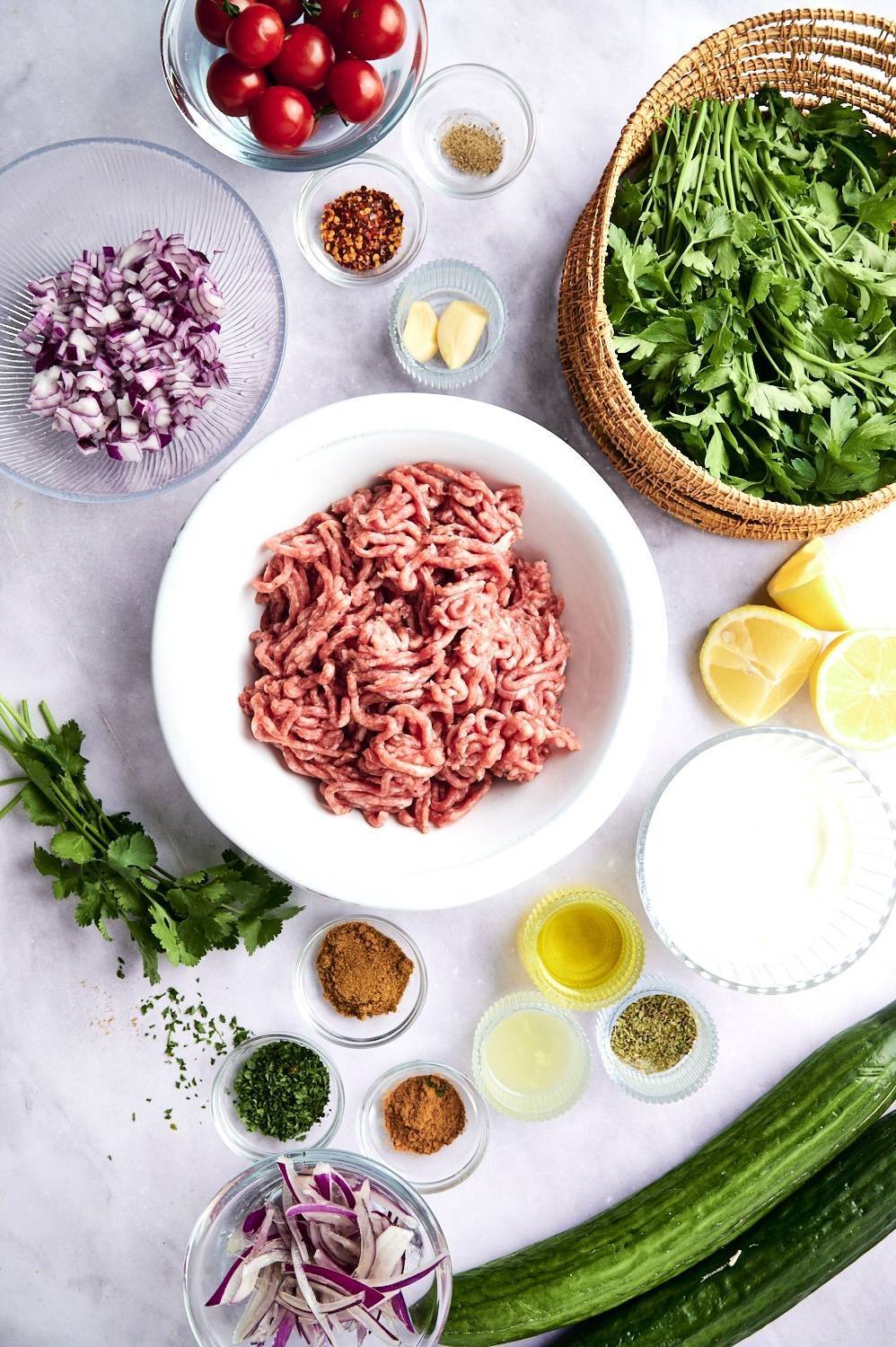 Ingredients for ground beef kofta bowls include lean beef, red onion, spices, lemon, garlic, tomatoes, cucumber and cilantro.