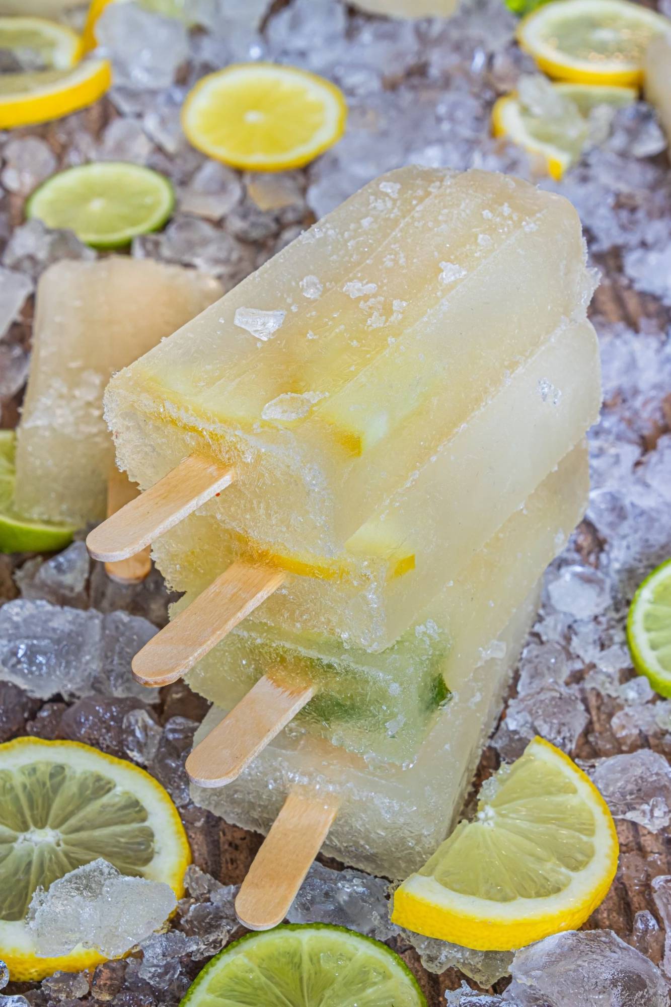 Three frozen lemon lime popsicles piled on ice, surrounded by fresh lemon and lemon slices.