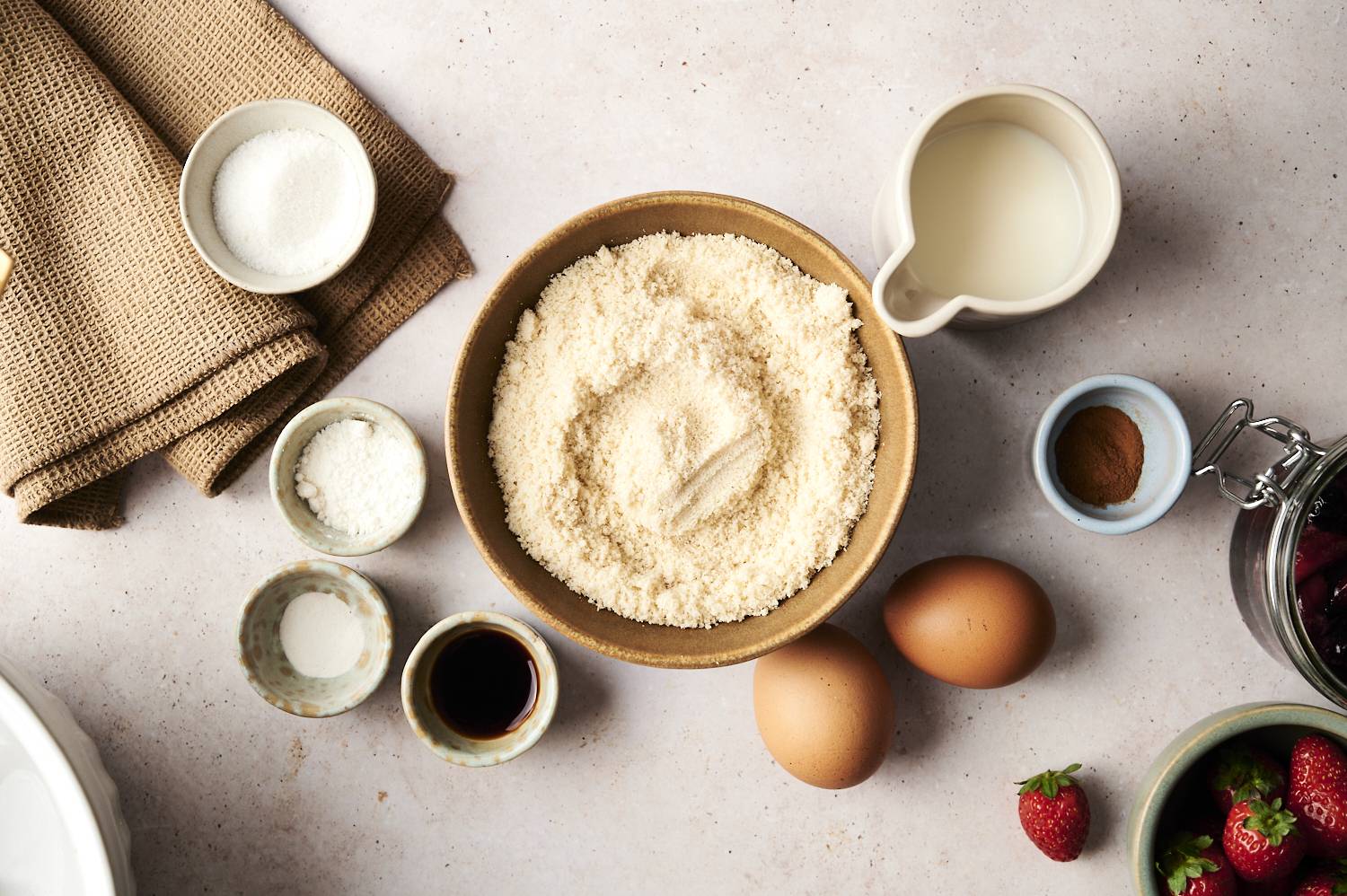 Low-carb flat ingredients including almond flour, eggs, milk, vanilla, sweetener, cinnamon and fresh strawberries.