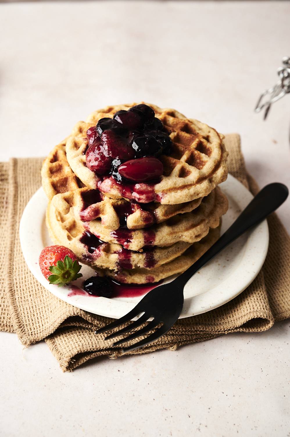 Close-up of tall low-carbon waffles sprinkled with berries and garnished with strawberries.