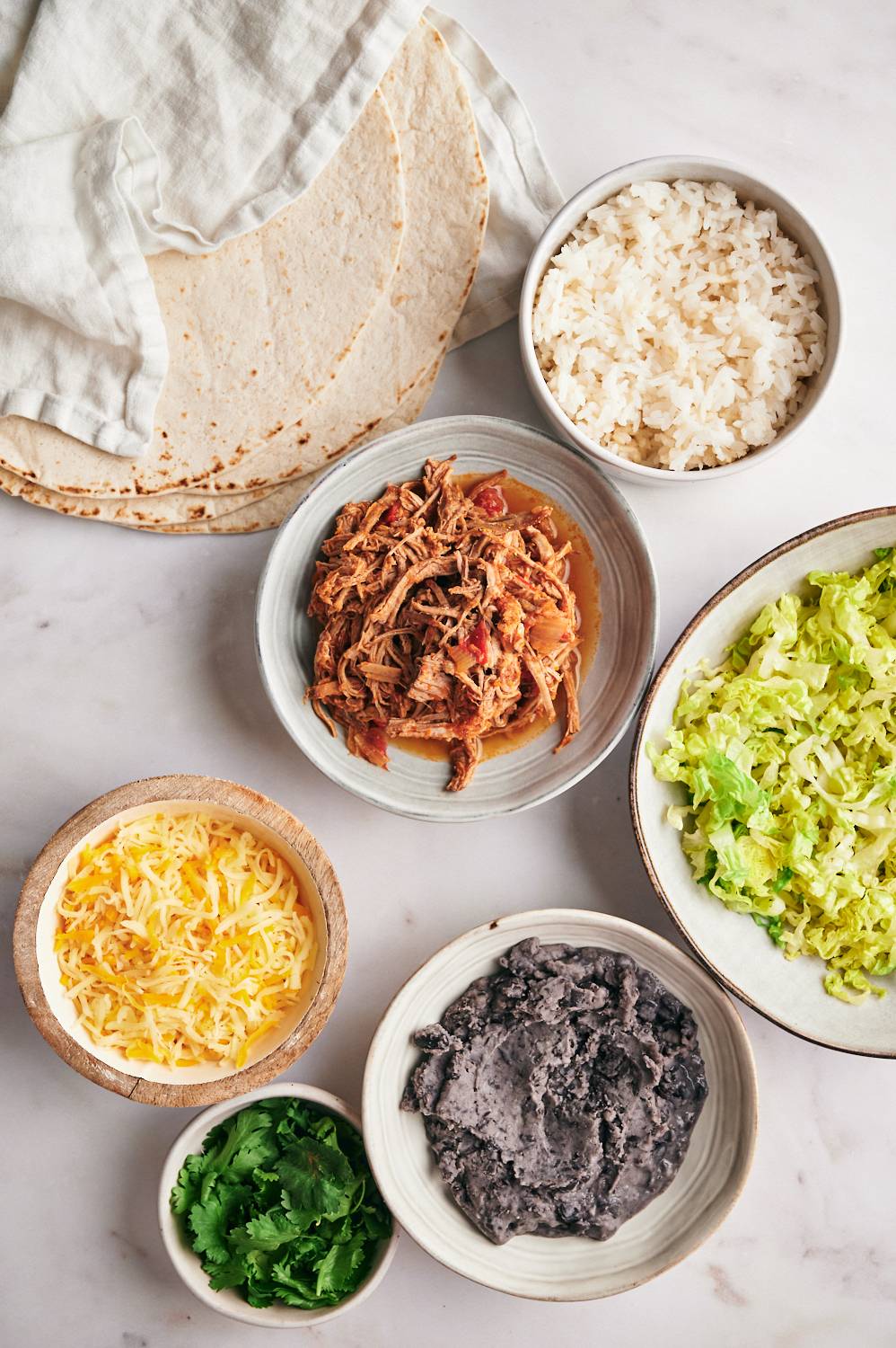 Ingredients for Machaca burritos, including chopped Machaca beef, beans, cheese, rice, coriander, lettuce and tortillas.