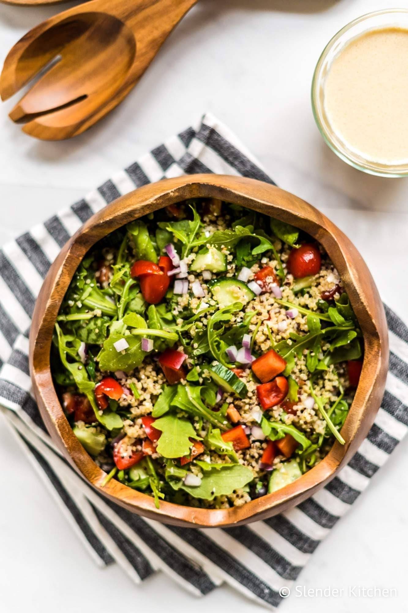 Quinoa salad bowl, Mediterranean style, including arugula, tomatoes, feta cheese and black olives, served in a wooden bowl.