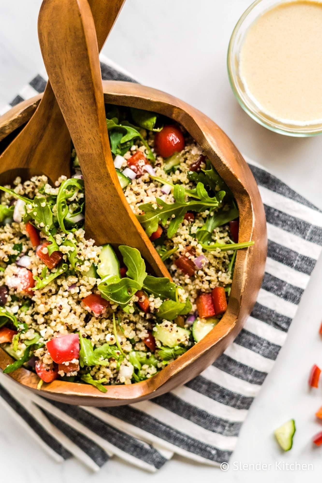 Quinoa bowl with feta cheese, olives, arugula, quinoa and hummus in a bowl with wooden utensils.