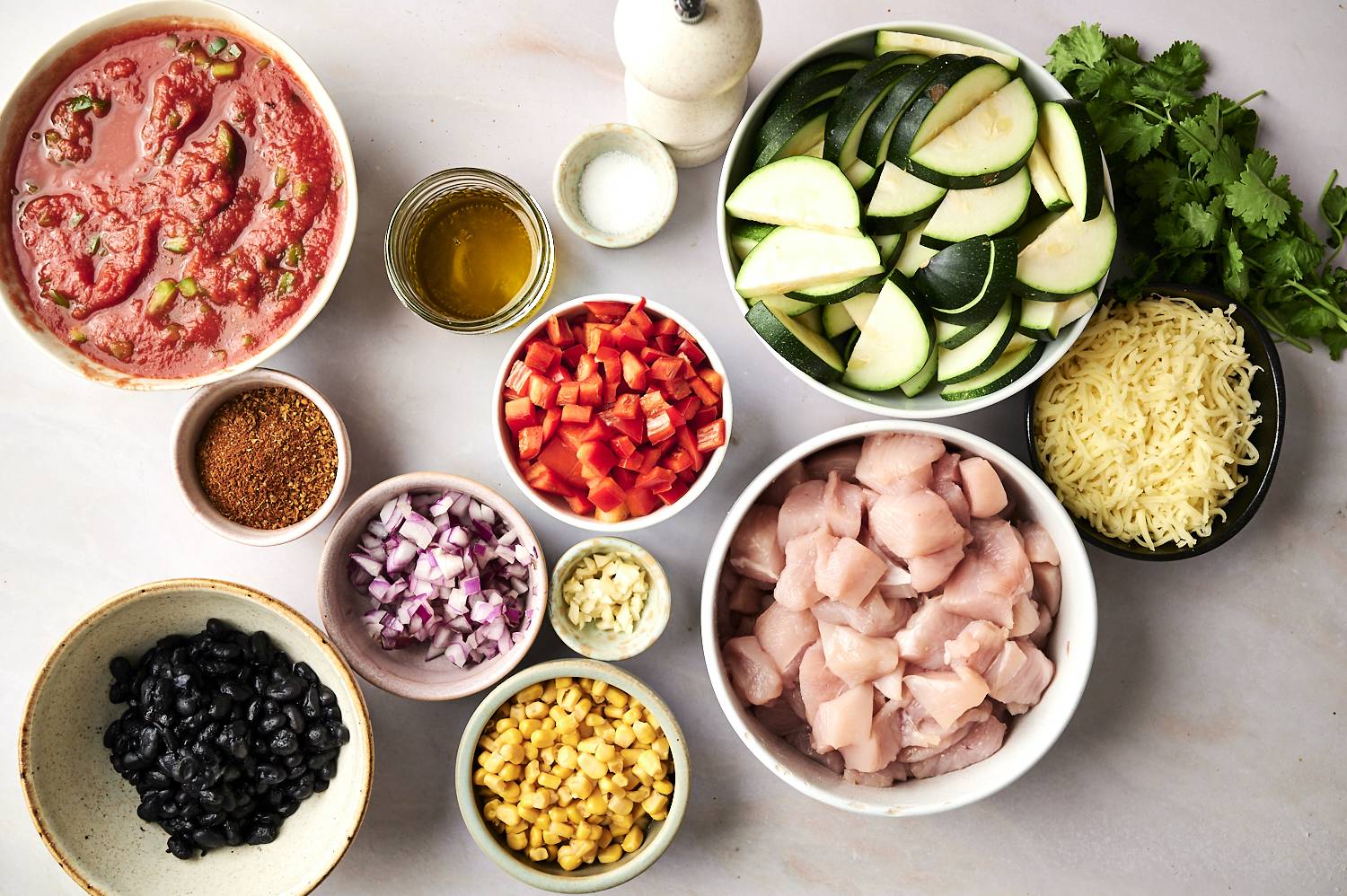 A variety of fresh ingredients to cook with: diced chicken, zucchini, peppers, black beans, corn, spices and sauces.
