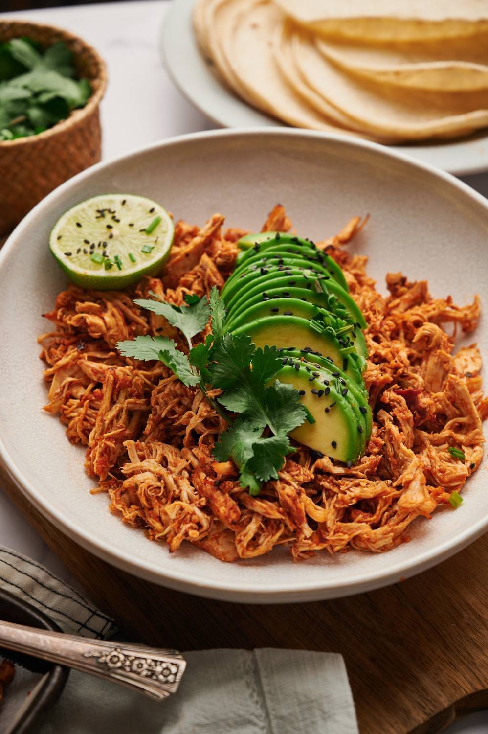 Chopped chicken in Mexican spices, tomatoes and chili peppers, served with avocado and lime in a bowl.