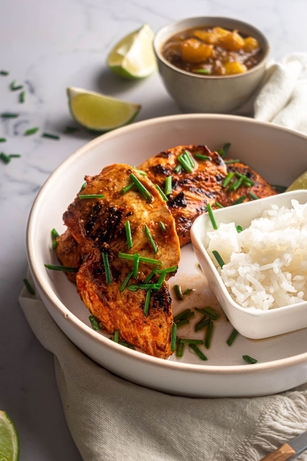 Crispy chili chicken breast, thinly sliced green onions on a plate with fresh lime and rice.