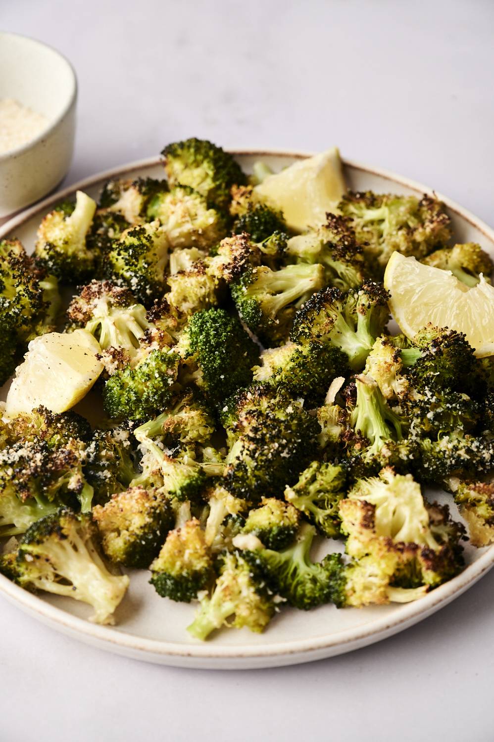 Oven-roasted broccoli flowers with crisp texture, with seasonings, garnish with lemon wedges on a plate.