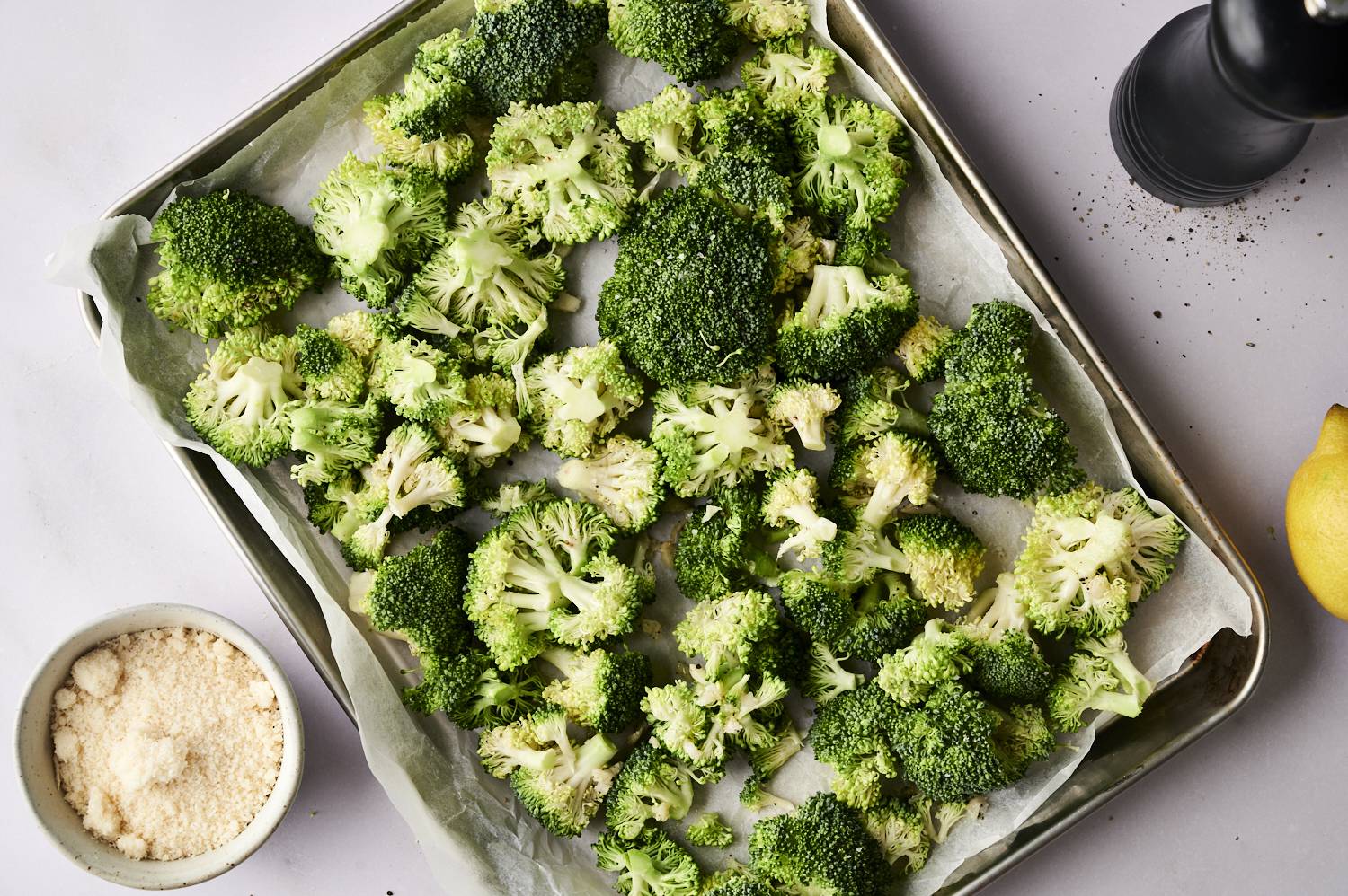 A plate of fresh broccoli flowers scattered on parchment paper, accompanied by a grated cheese and lemon.
