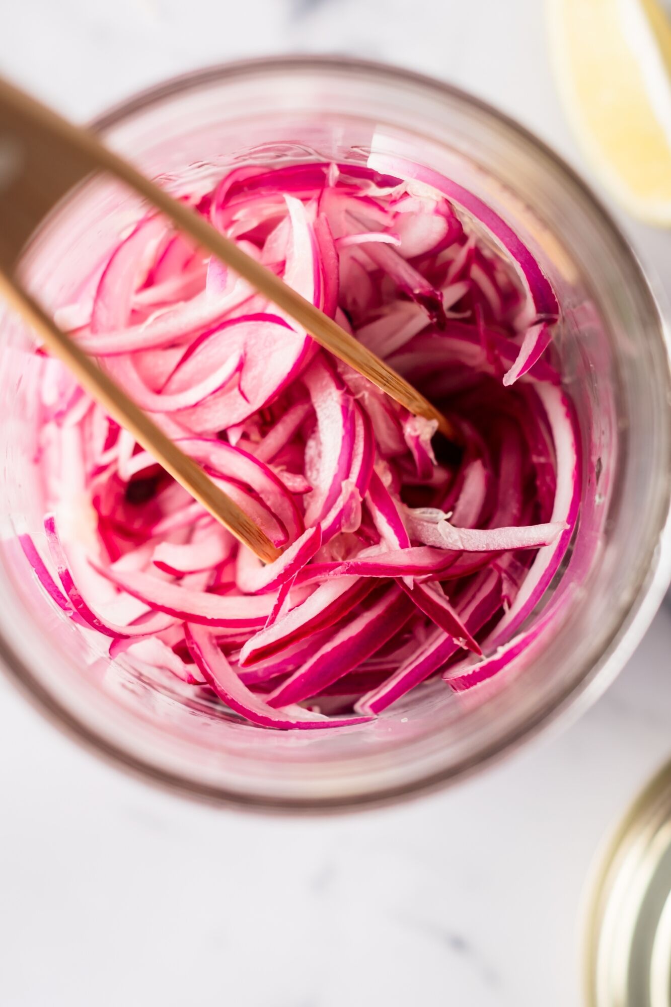 Pickled onions with thinly sliced red onions in a jar with lime juice, vinegar, salt, and peppercorns with cilantro on the side.