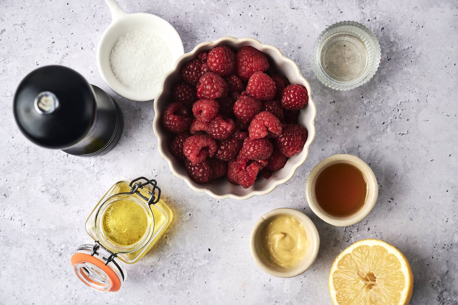 A bowl of fresh raspberries surrounded by olive oil, honey, mustard, salt, lemon and vinegar, with texture above.