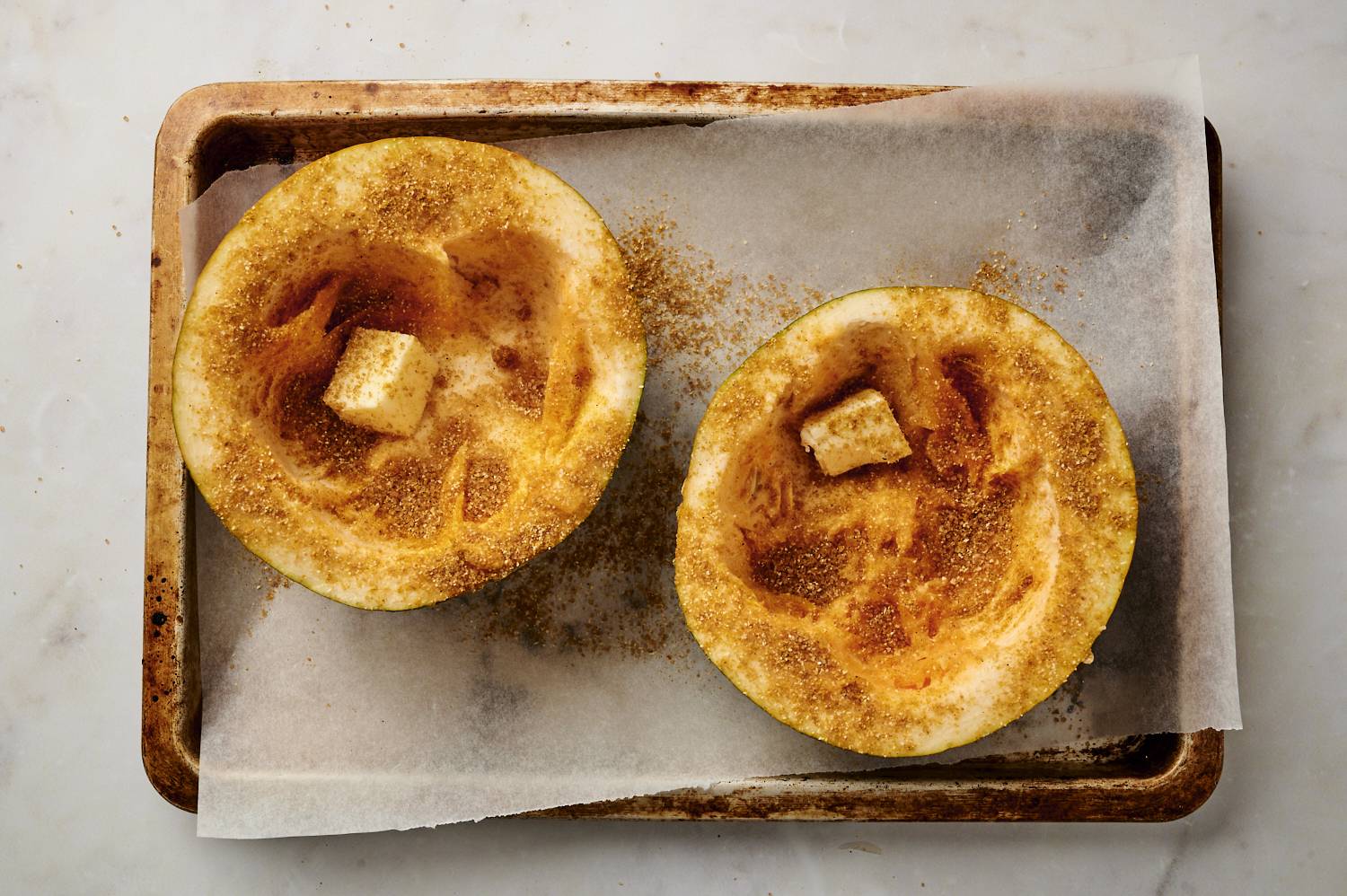Sliced acorn squash with butter, cinnamon, brown sugar, and spices on a baking sheet.