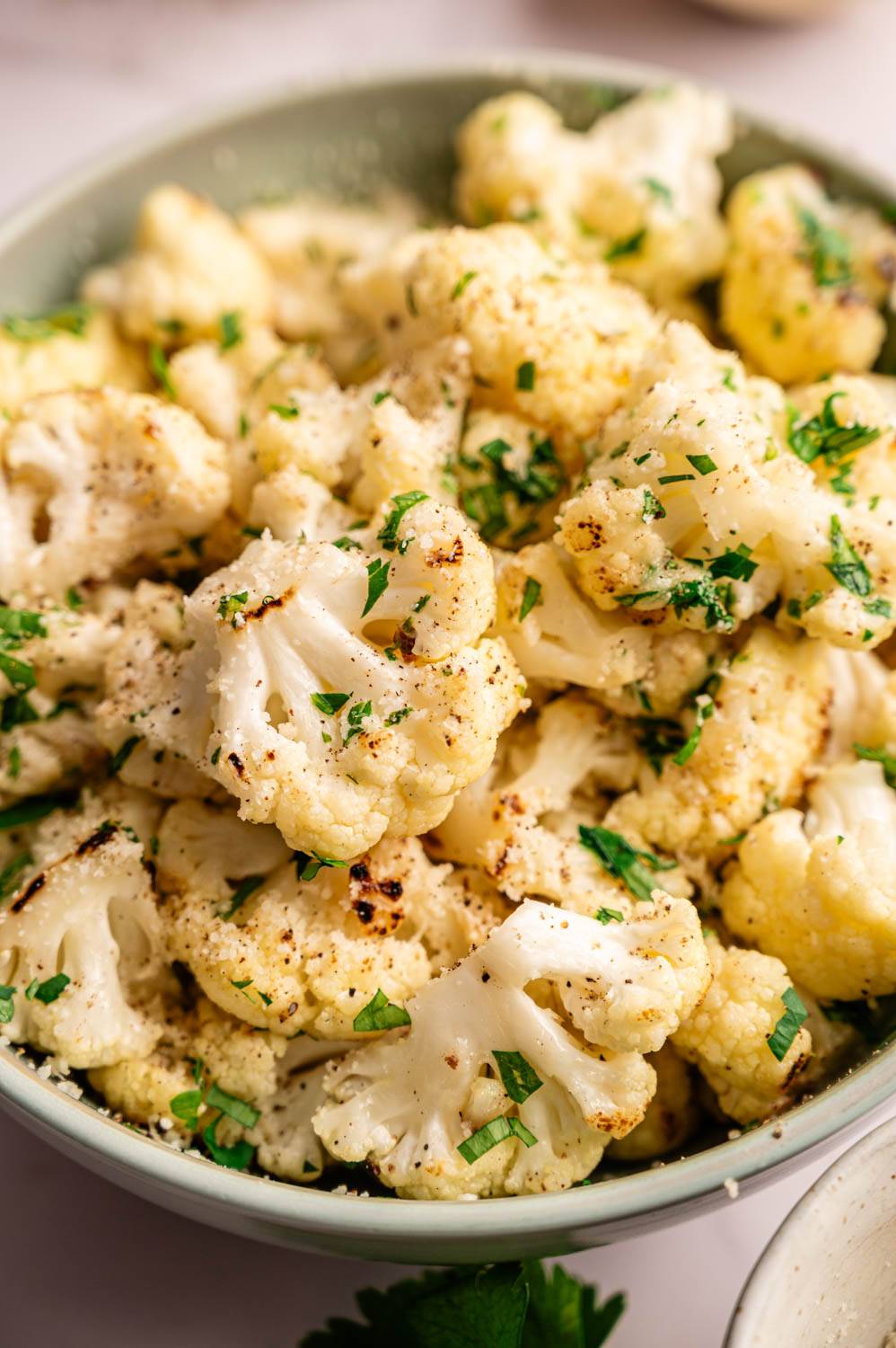 Close-up of roasted cauliflower florets in a bowl, light brown, garnished with chopped parsley.