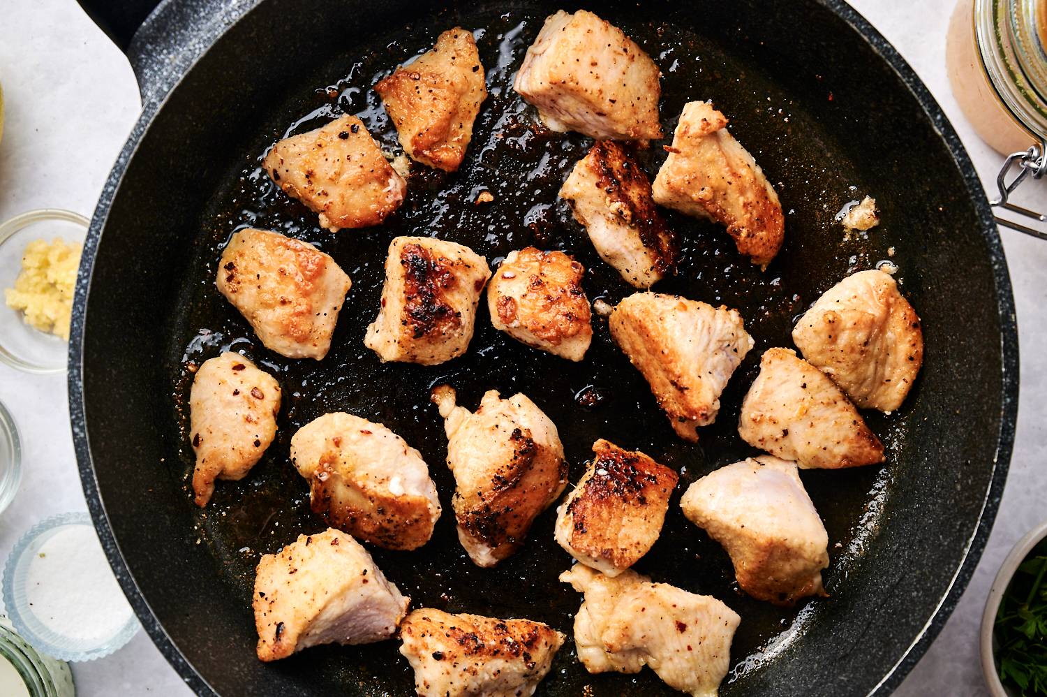 Lemon pepper chicken breast chunks cooking in a cast iron skillet with golden brown edges.