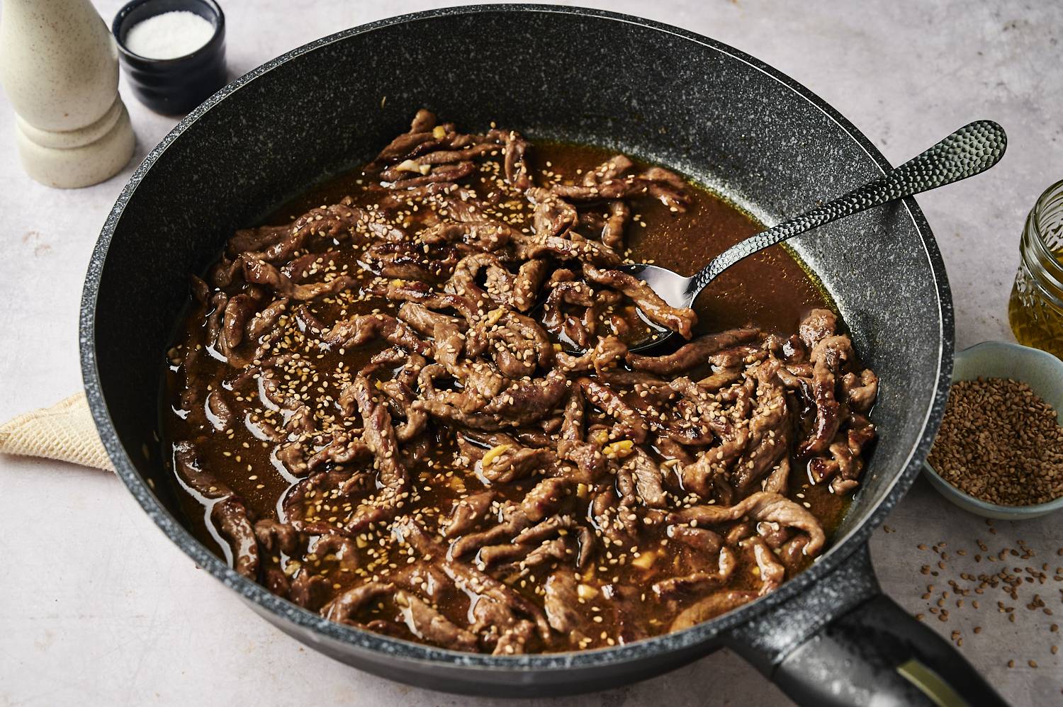 Beef strips simmering in a thick sesame sauce and sprinkled with sesame seeds in a skillet.