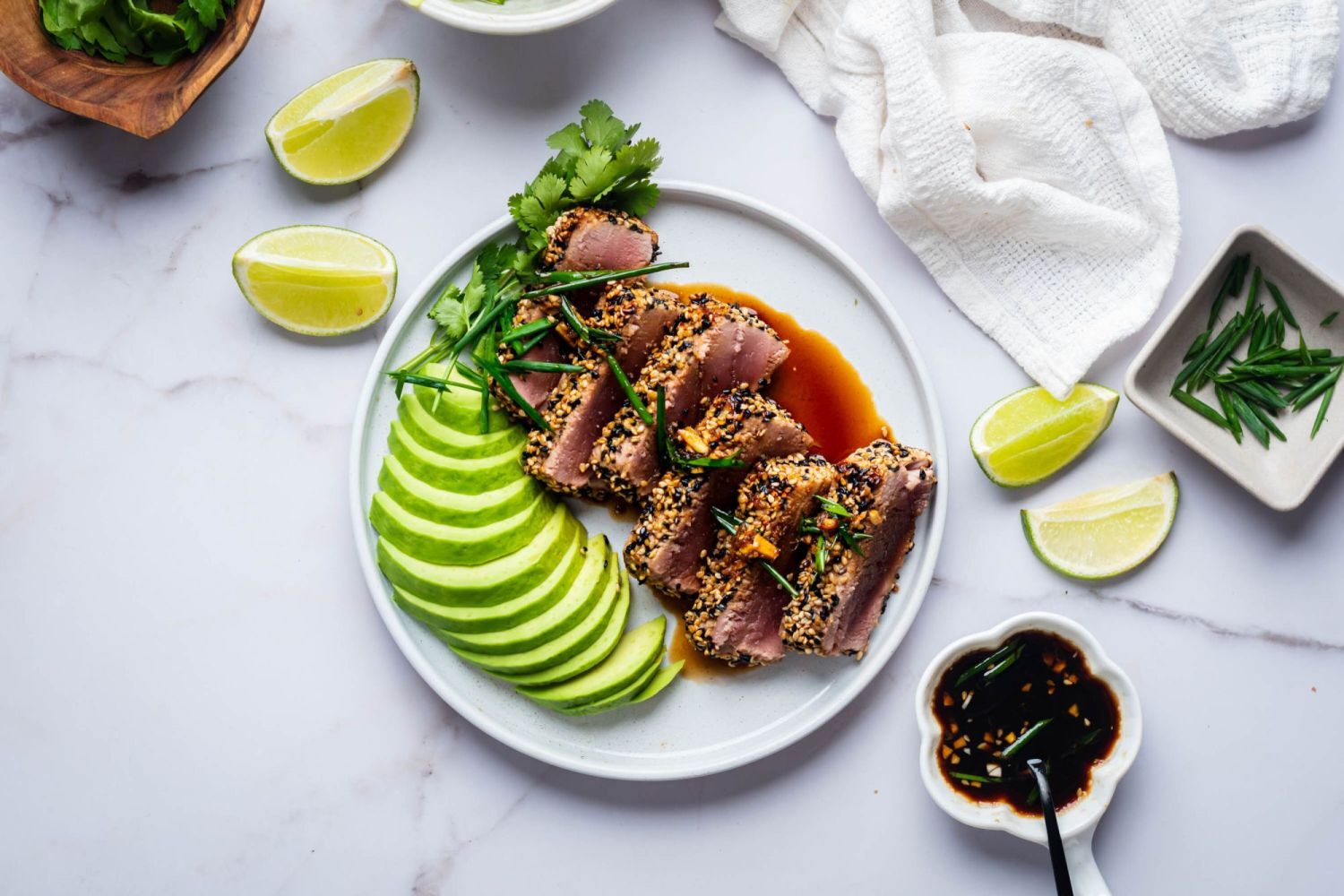 Sesame seared tuna with soy sauce and avocado on a white plate with lime on the side.