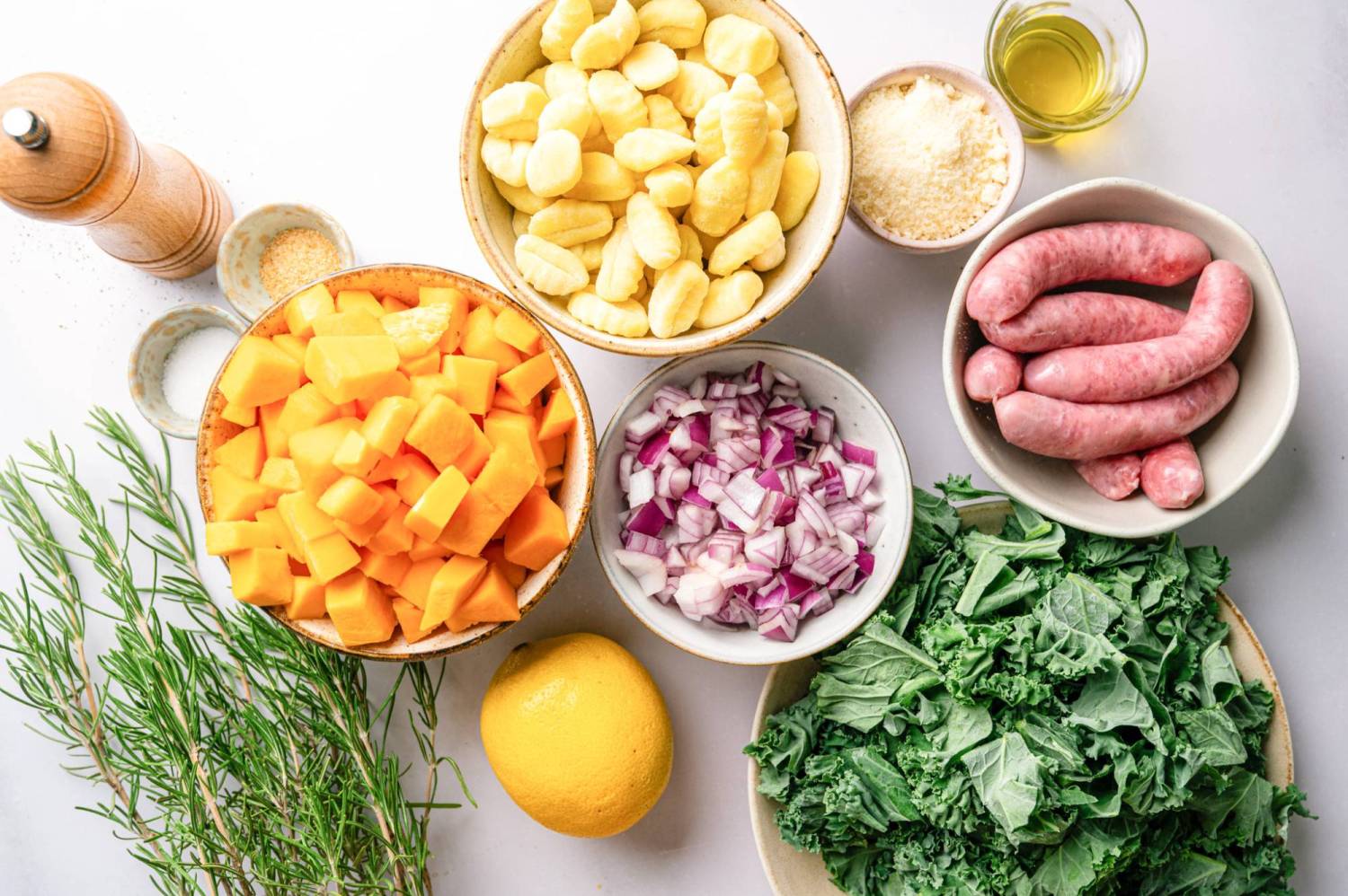 Ingredients for sheet pan gnocchi and sausage including butternut squash, red onion, rosemary, and kale.