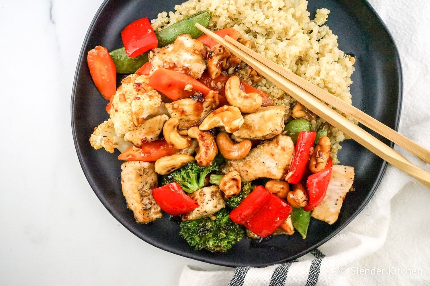 Healthy cashew chicken with vegetables on black plate with chopsticks.