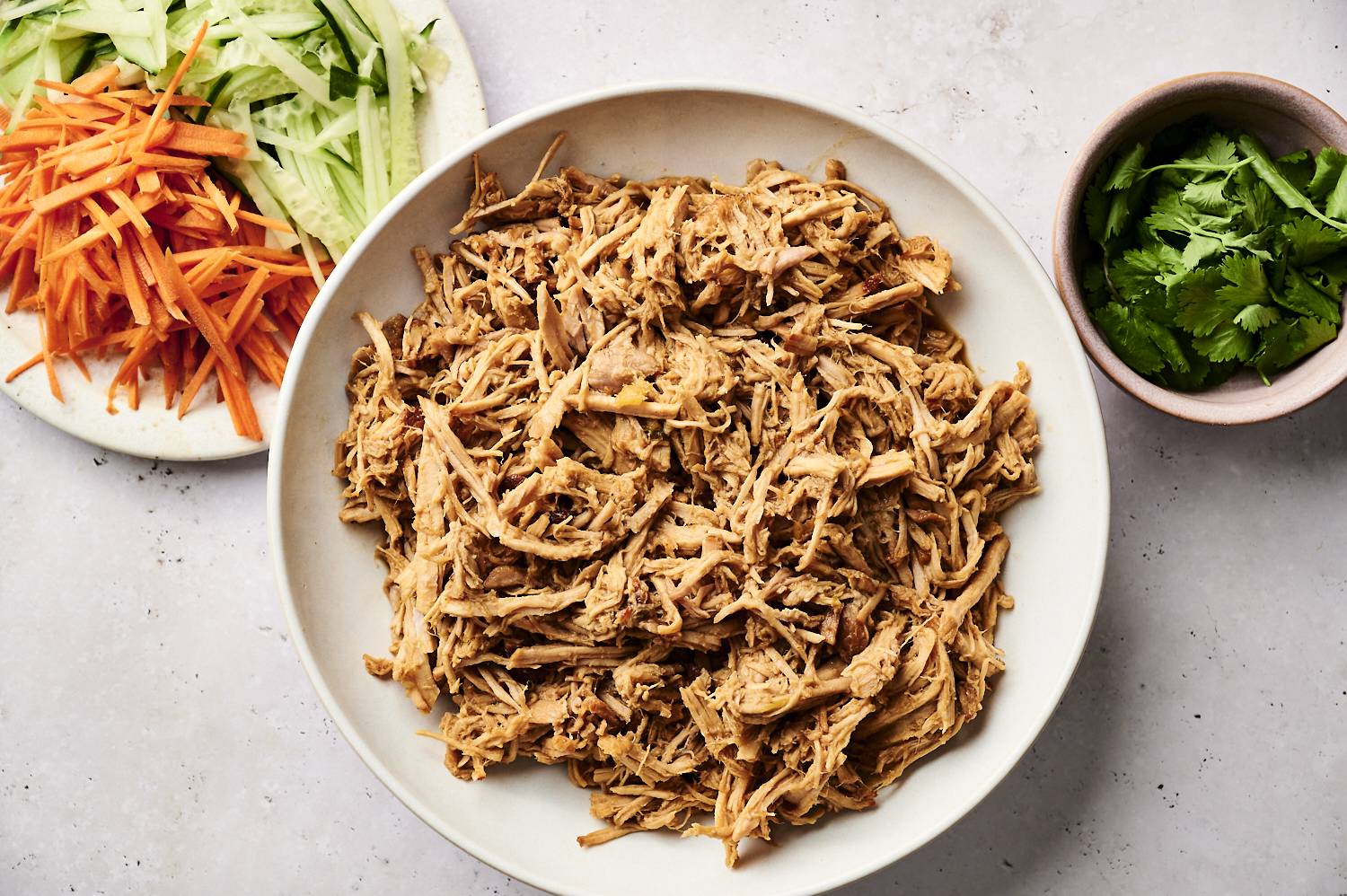 A bowl of thinly sliced ​​meat surrounded by thinly sliced ​​cucumbers, carrots and fresh coriander.