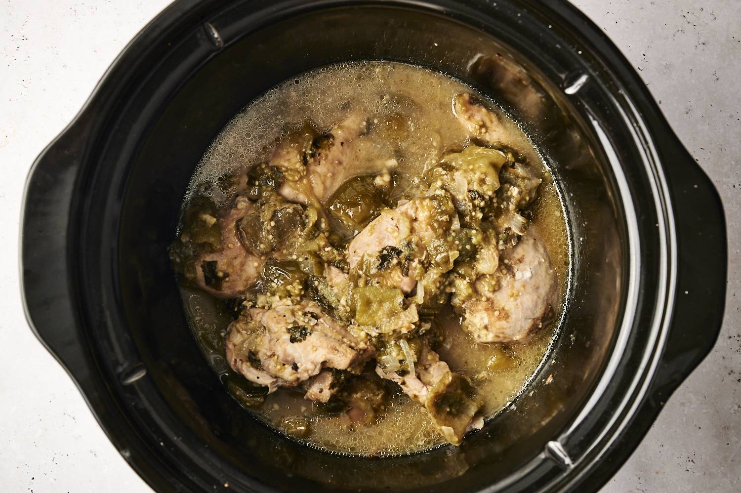 Cooked chicken and tomatillos in a slow cooker, stewed to tender perfection in a flavorful chile verde sauce.