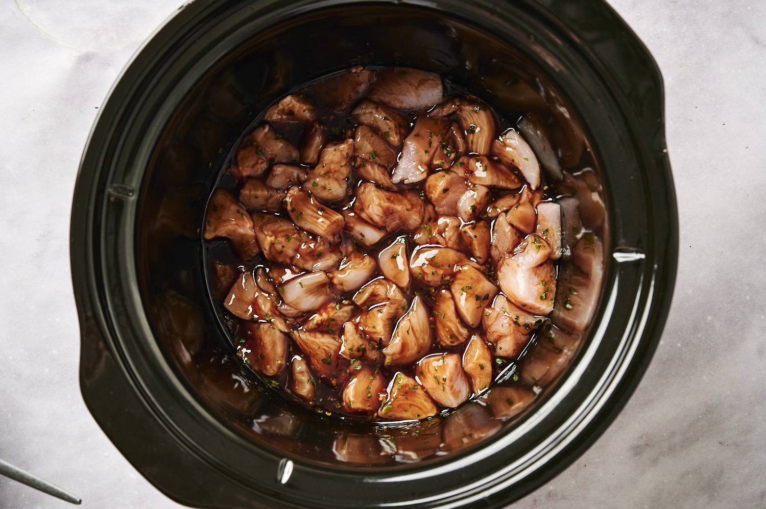 Slow cooker with chopped chicken breast covered in honey garlic sauce.