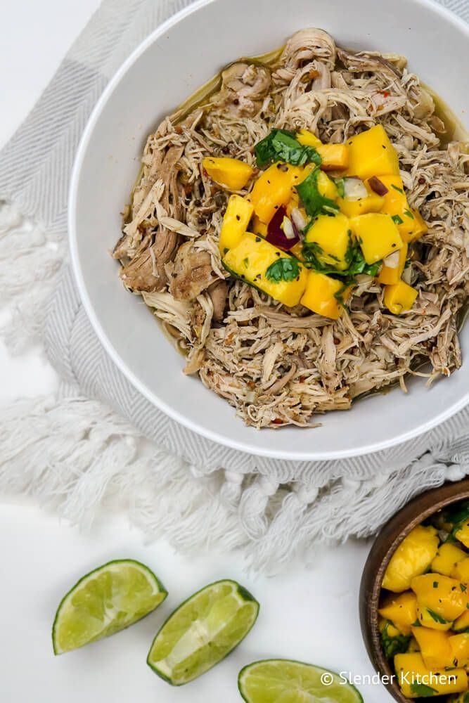 Crockpot bastard chicken in a bowl with sliced ​​lime and mango salsa.