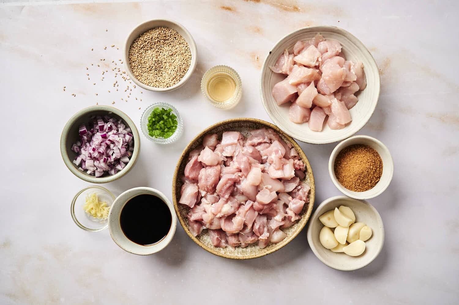 Ingredients for slow cooker Korean chicken including chicken, garlic, brown sugar, onions, soy sauce, ginger, and sesame seeds.
