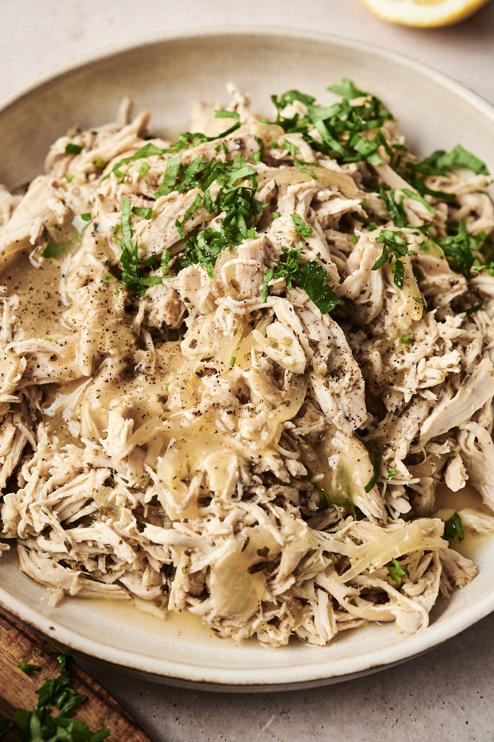 A close-up of shredded slow-cooked chicken with onions, garlic, and herbs, garnished with fresh parsley and black pepper.