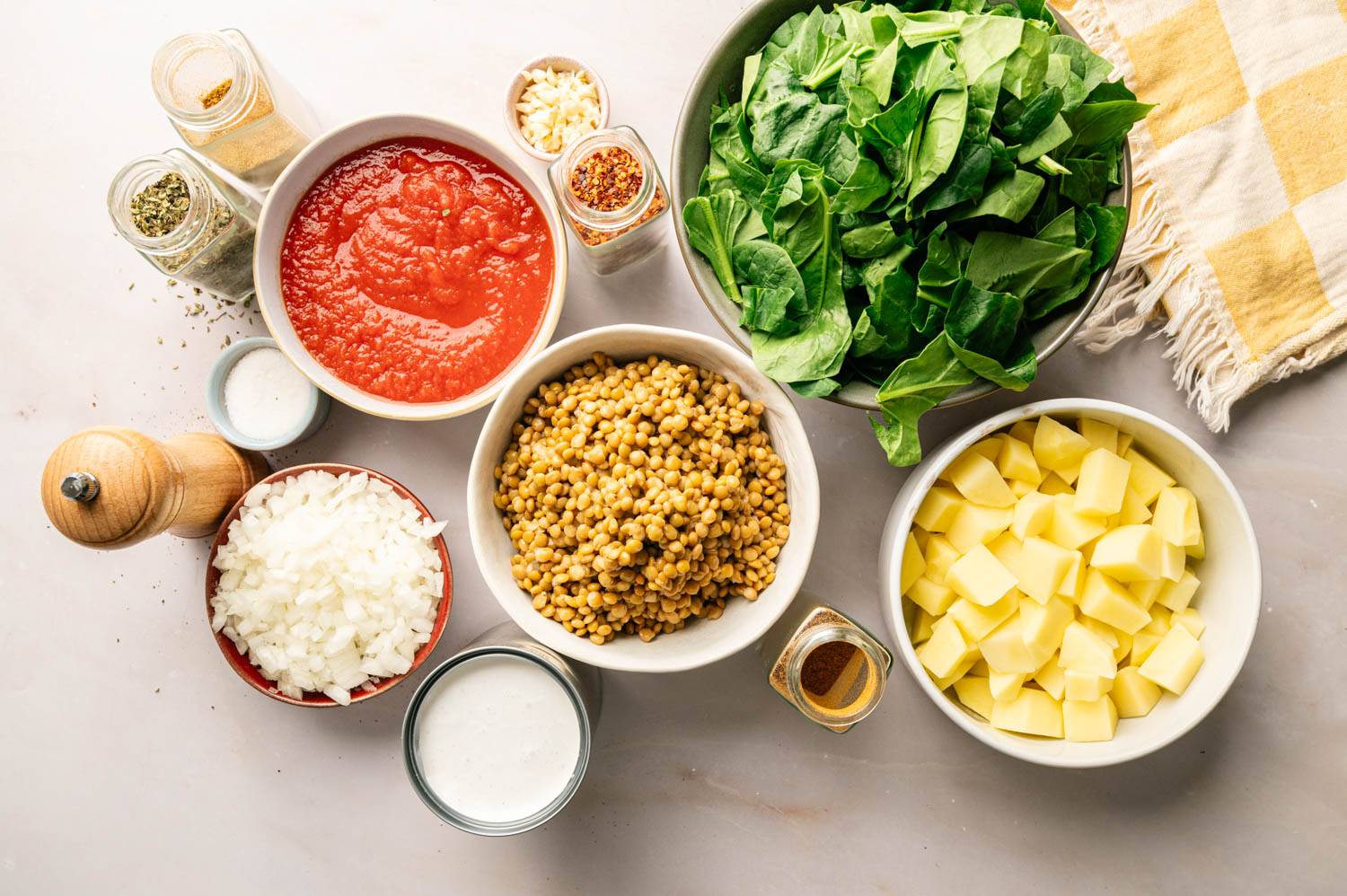 Ingredients for slow cooker Madras lentils arranged on a countertop, including lentils, potatoes, spinach, crushed tomatoes, coconut milk, onions, garlic, and seasonings.