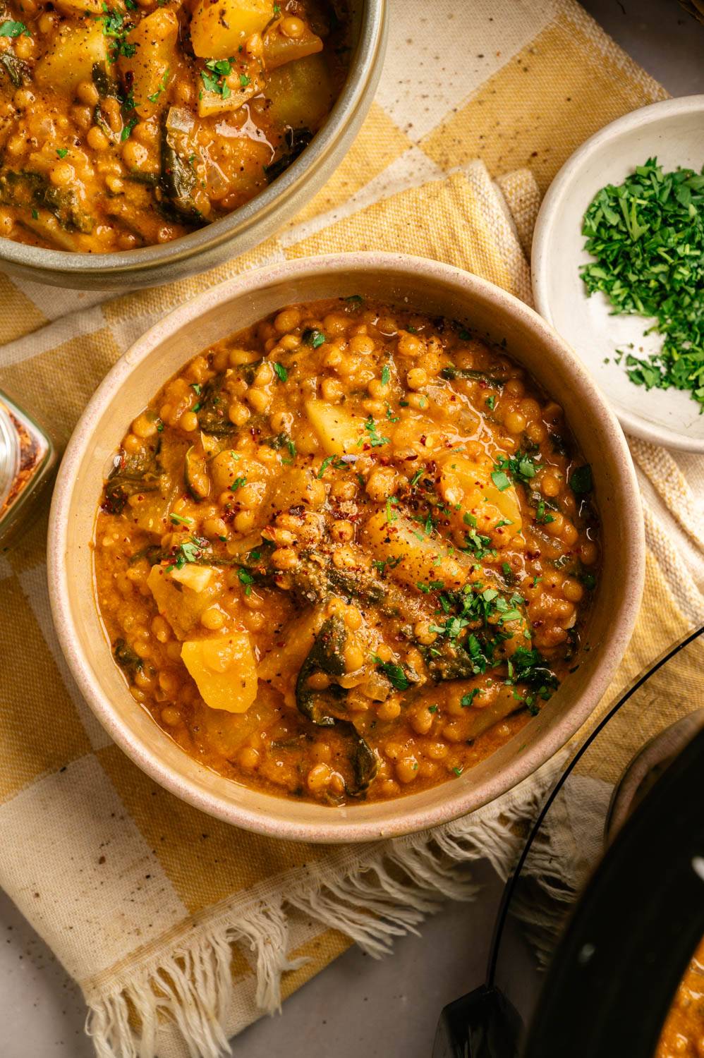 Overhead shot of a bowl of slow cooker Madras lentils topped with fresh herbs and red pepper flakes on a yellow striped kitchen towel.