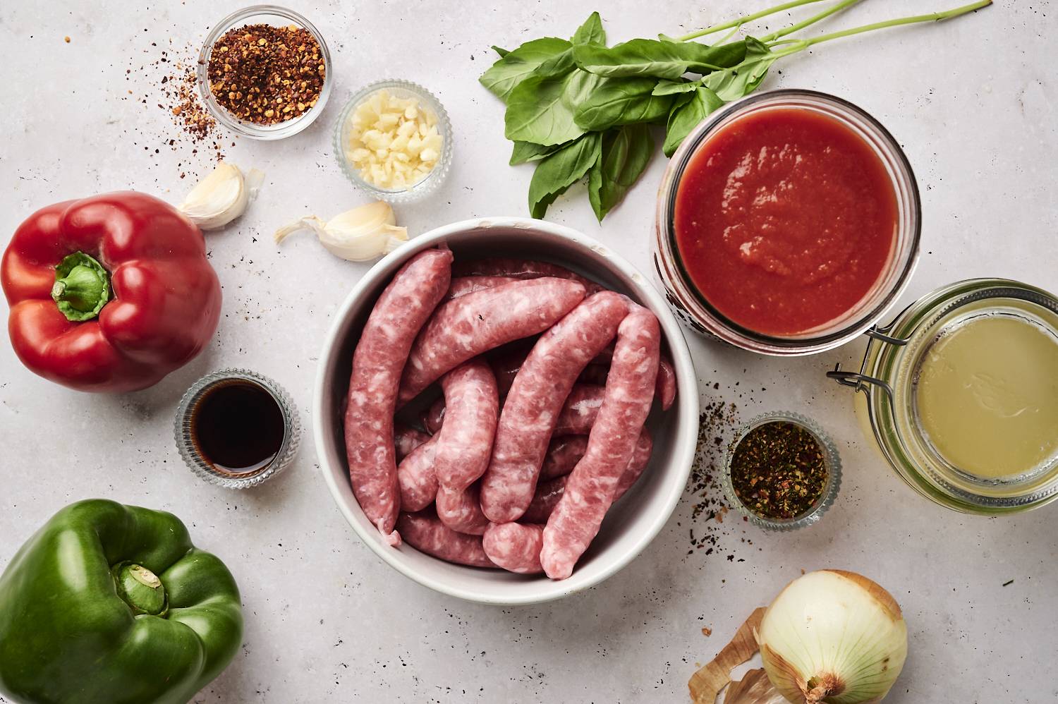 Raw ingredients for slow cooker sausage and peppers, including sausages, bell peppers, garlic, basil, tomato sauce, and spices.