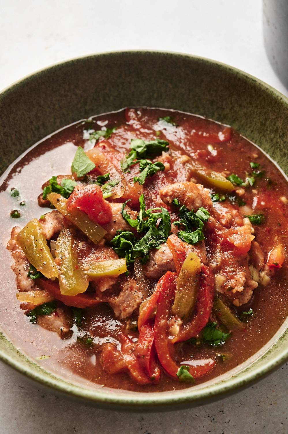 Slow cooker sausage and peppers in tomato sauce, served in a bowl and garnished with fresh herbs.