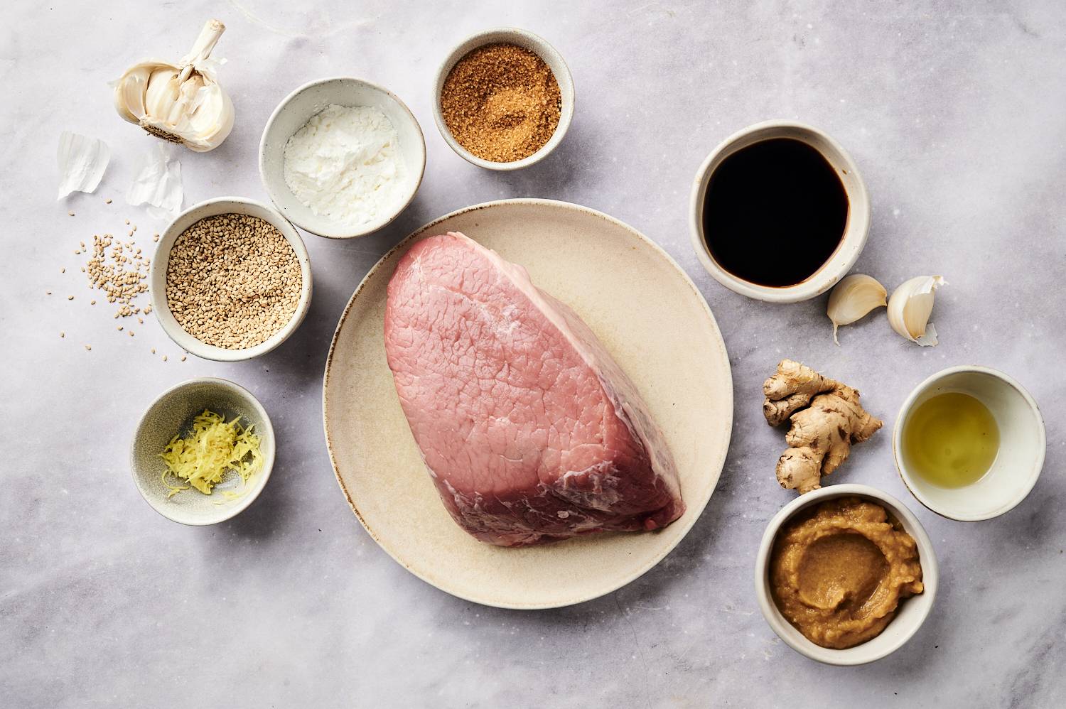 Raw roast surrounded by sesame beef ingredients like garlic, ginger, soy sauce, and seasonings.