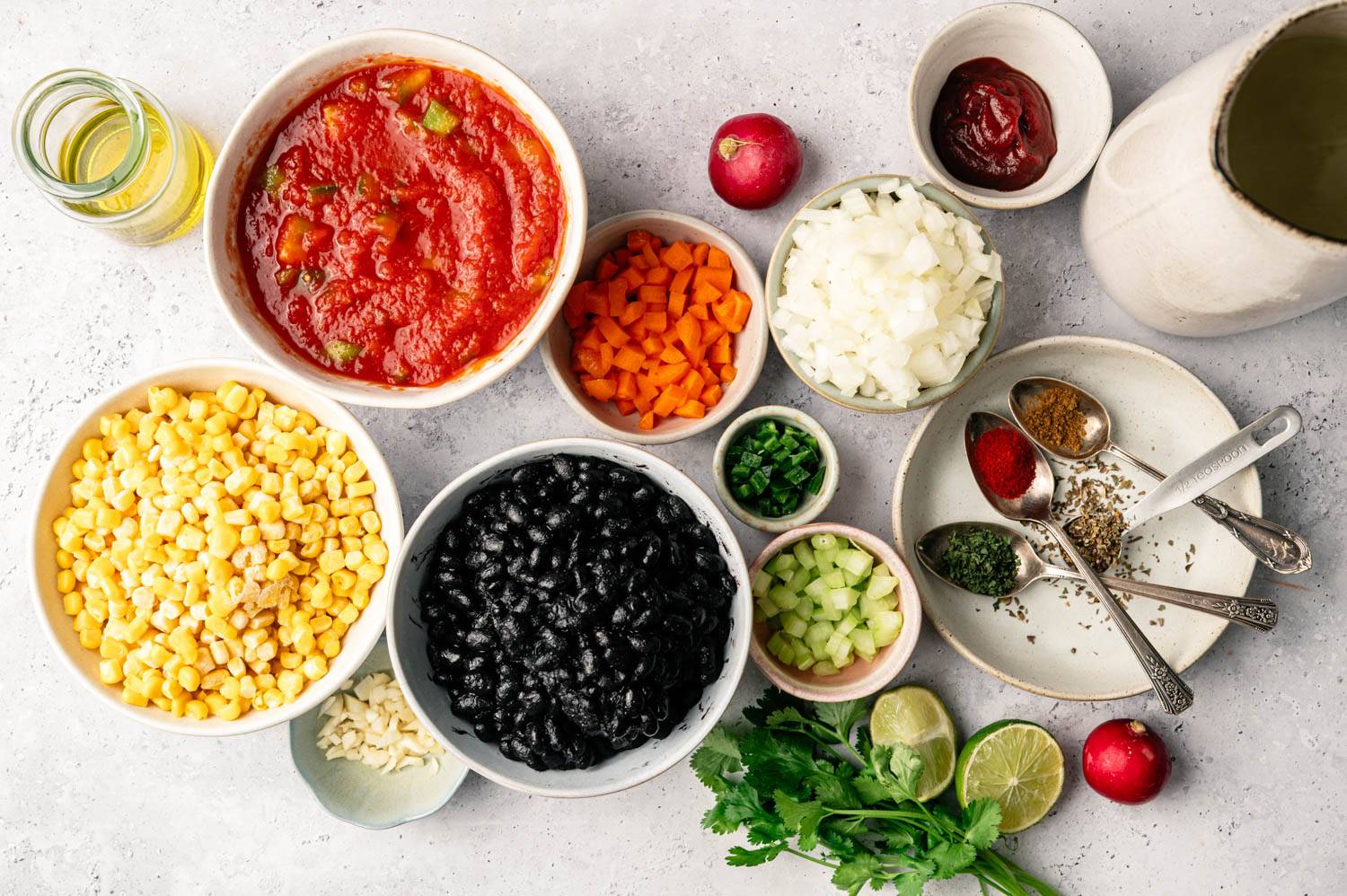 Colorful ingredients are neatly arranged on the bright surface to create vibrant recipes. Includes a bowl of tomatoes, corn, black beans, spices and fresh herbs.