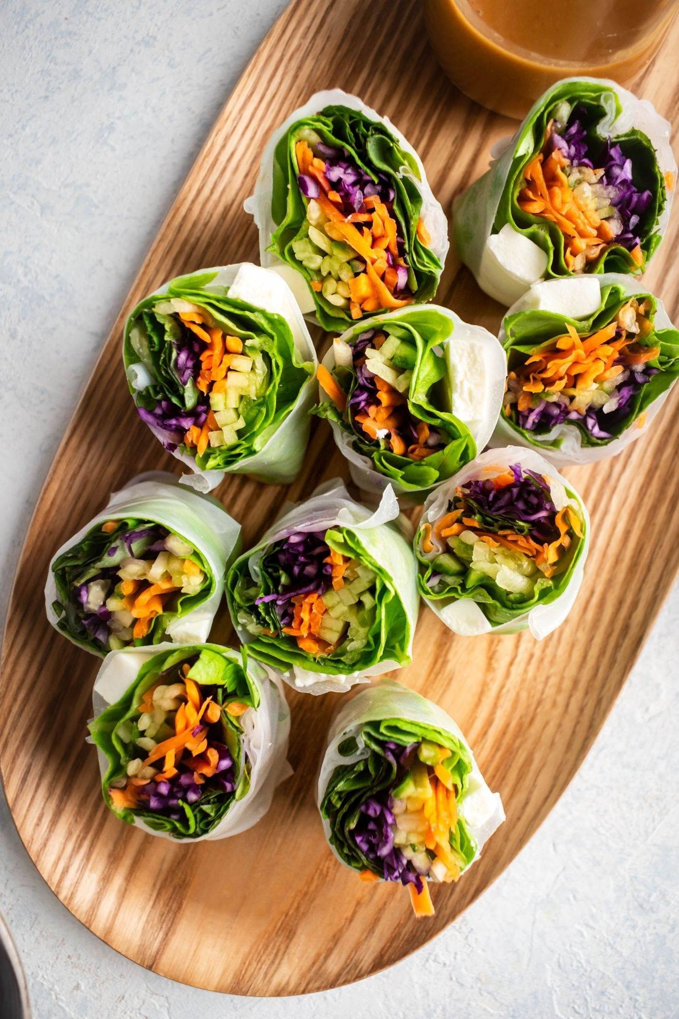 Tofu spring rolls with carrots, lettuce, cabbage and cucumber served with peanut sauce on wooden tray.